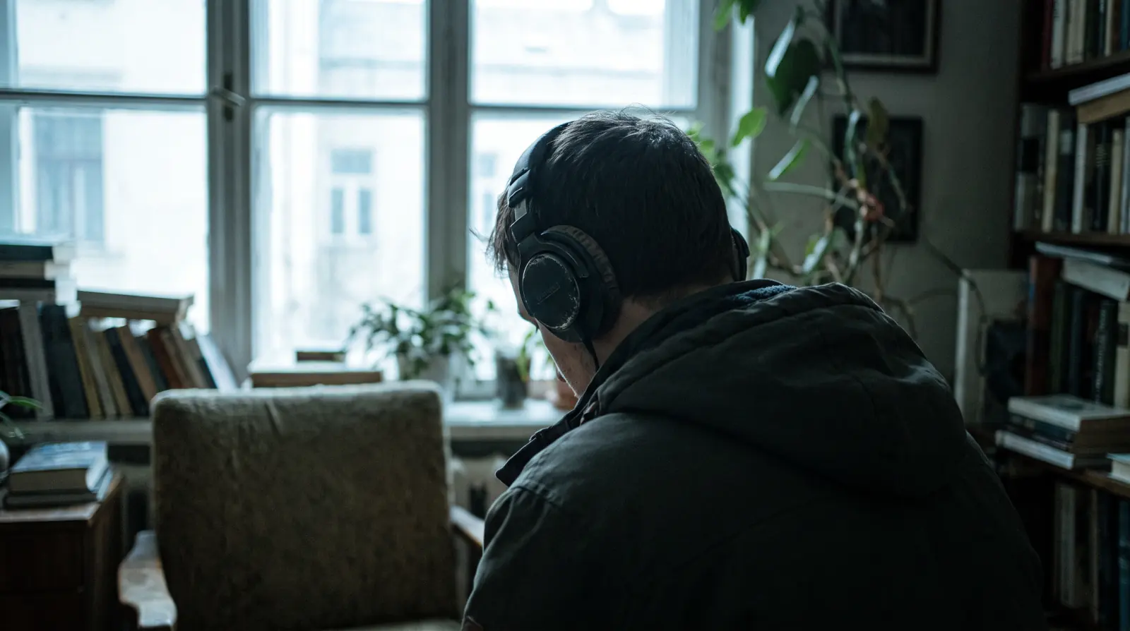 A person seen from behind wearing headphones beside a window